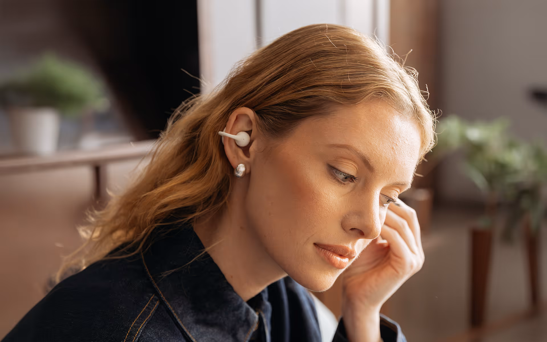 Woman with blonde hair wearing white wireless earbuds and a black top, touching one earbud softly.