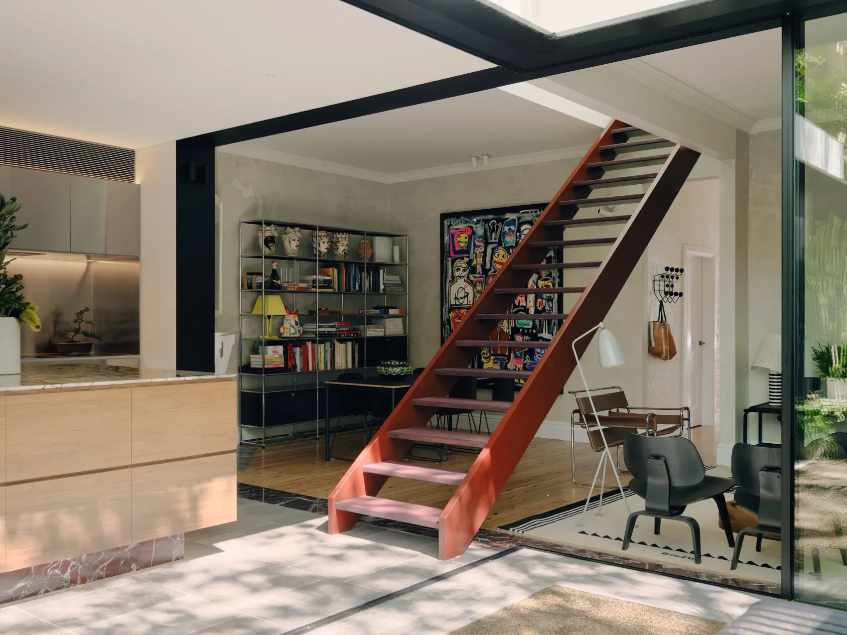 Modern living space with red staircase, bookshelf with decorative items, and glass wall showing outdoor light.