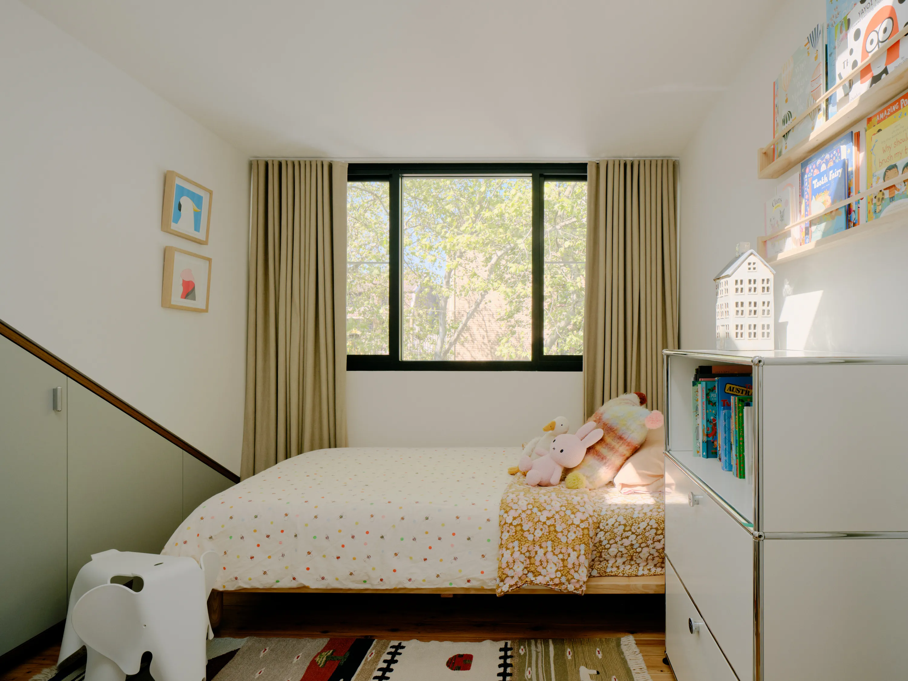 Contemporary bedroom with built-in storage, children's bookshelf, and large window with natural light.