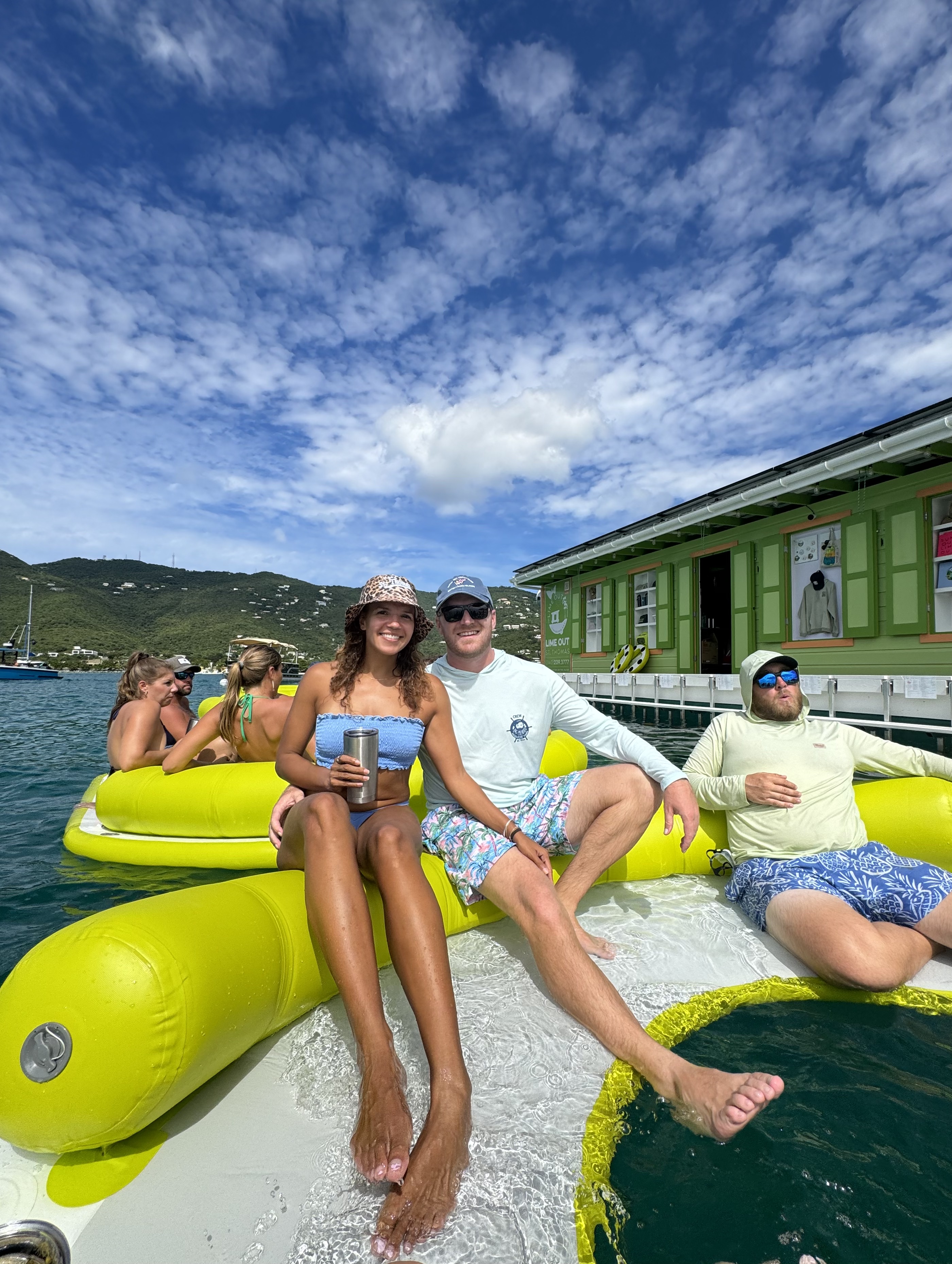 Woman in sunglasses holding a cup on a boat with turquoise water and green hills in the background.