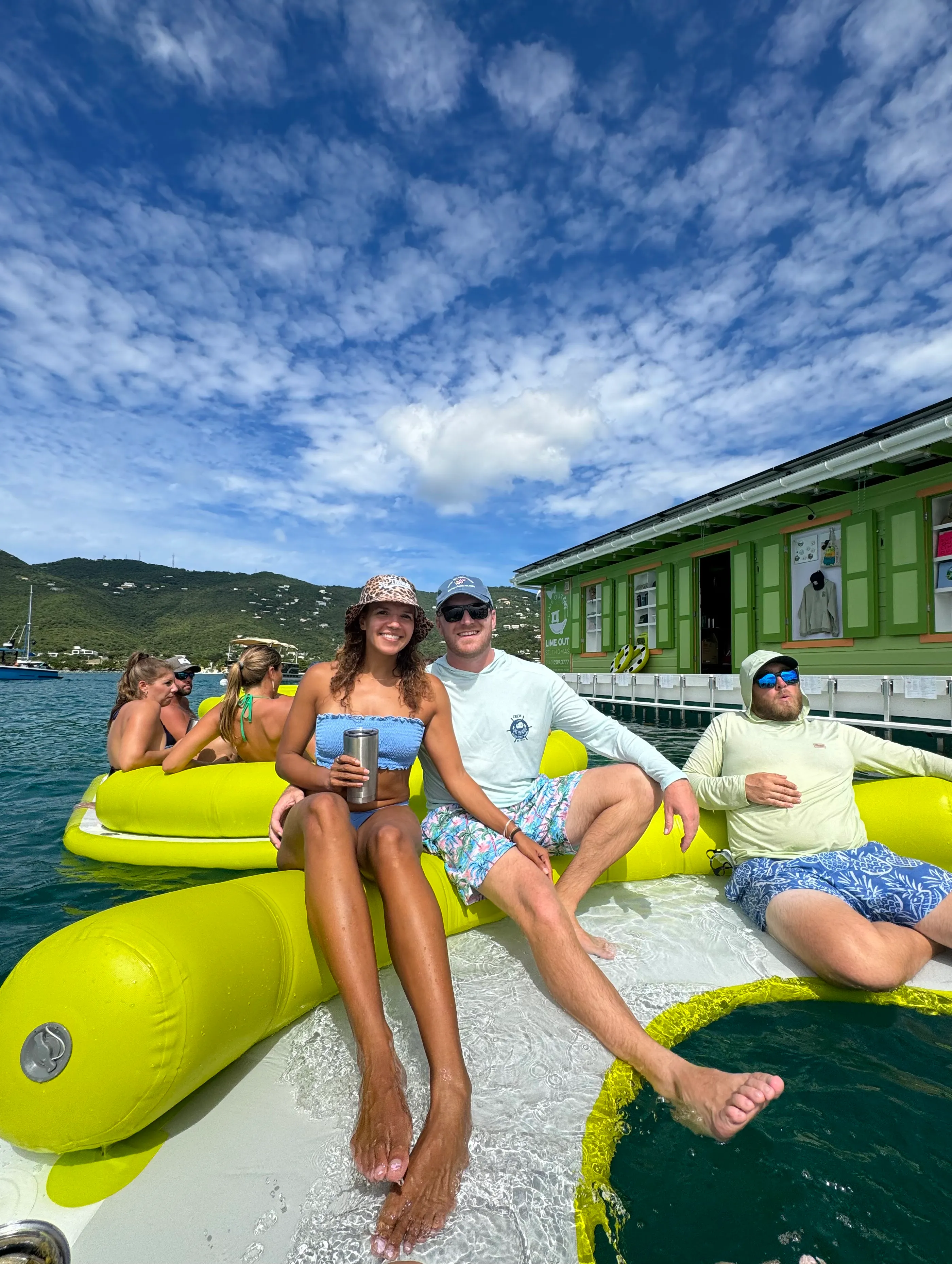 Woman in sunglasses holding a cup on a boat with turquoise water and green hills in the background.