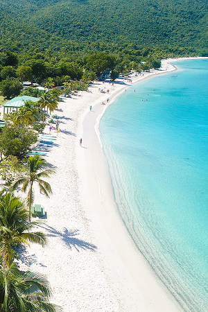 Curved white sandy beach with clear turquoise water and lush green forest in the background.