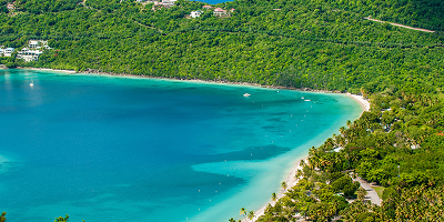 Aerial view of a tropical beach with turquoise water and dense green forest surrounding it.