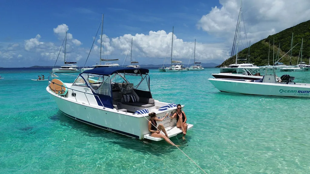 Woman wearing sunglasses reading a book while relaxing on a white boat by clear blue water.