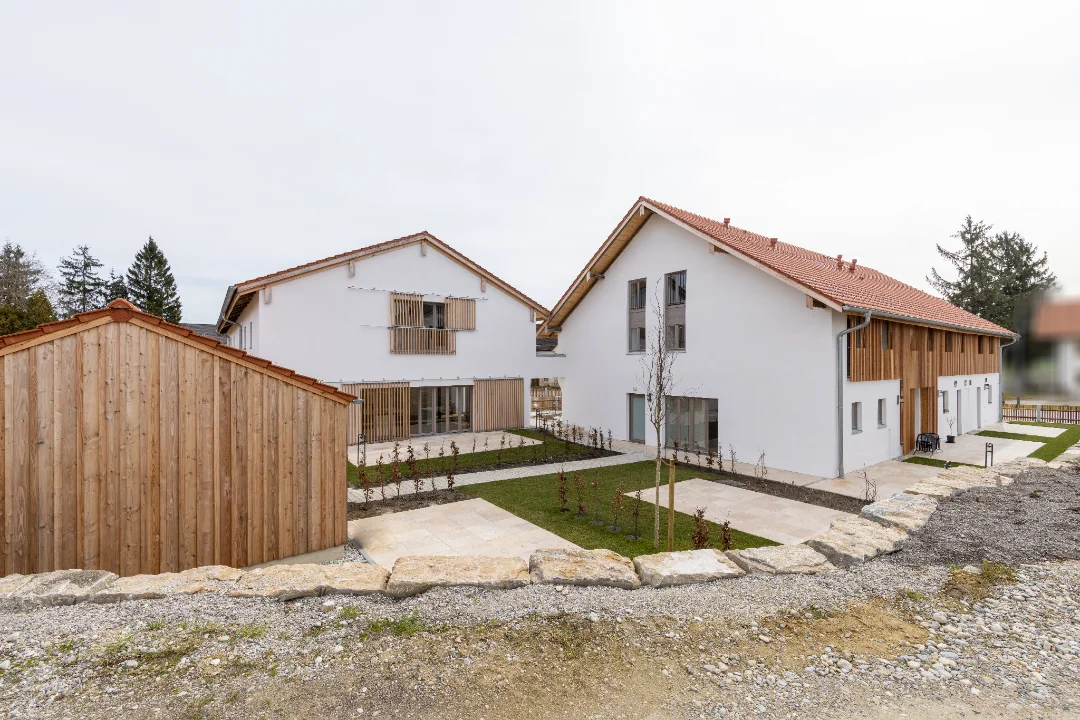 Moderne weiße Häuser mit Holzverkleidung und roten Ziegeldächern in einer gepflegten Gartenanlage.