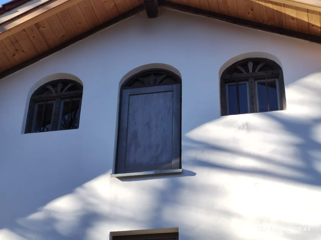Weiße Hauswand mit drei kleinen bogenförmigen Fenstern, ein Fenster ist zugemauert.
