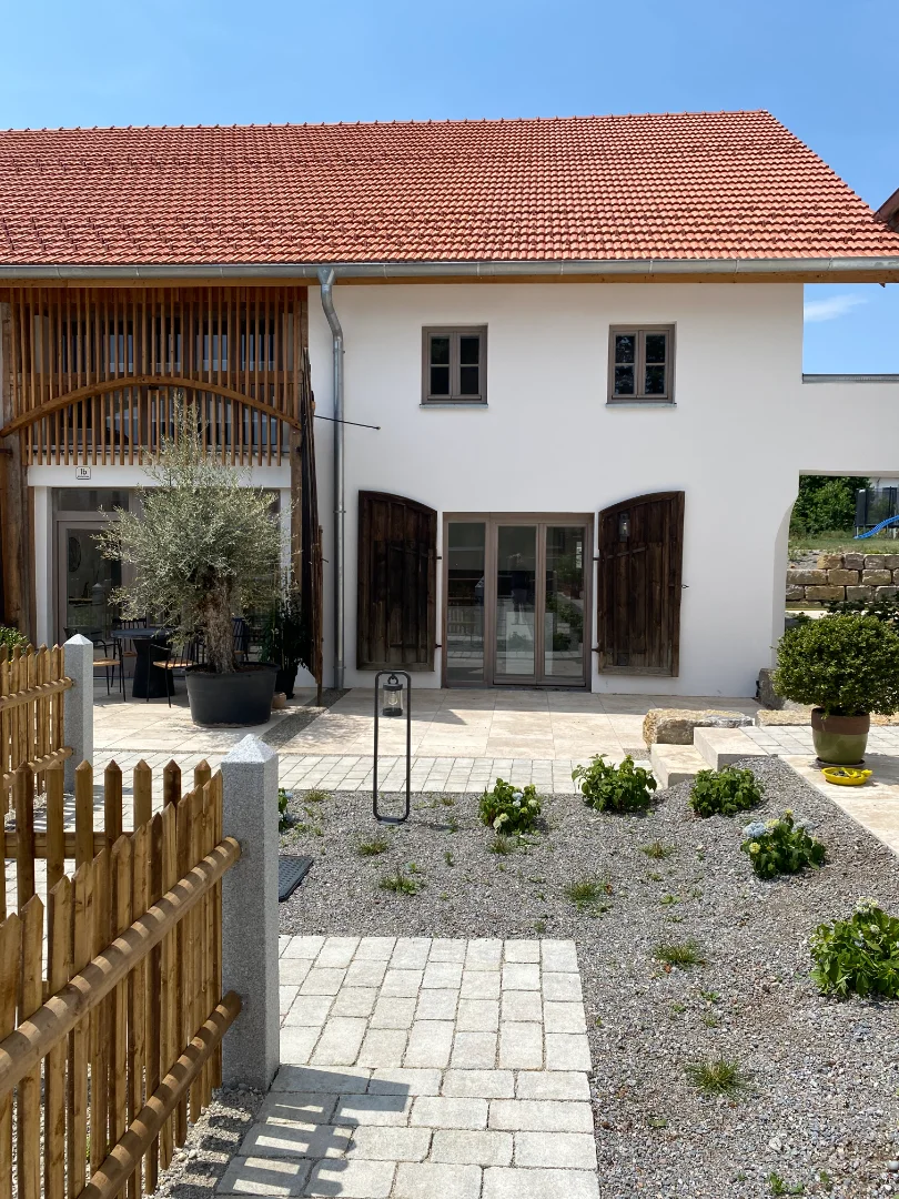 Haus mit rotem Ziegeldach, weißen Wänden, Holzveranda, Garten und gepflastertem Weg.
