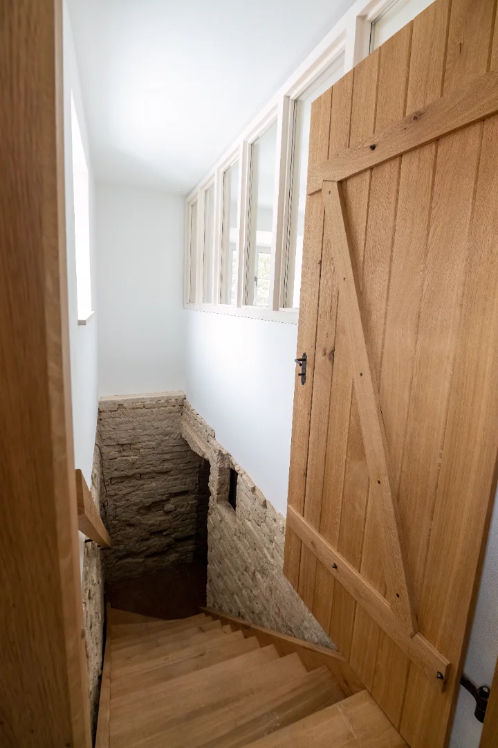 Holztreppe führt hinunter in einen Keller mit Steinwänden und offener Holztür.