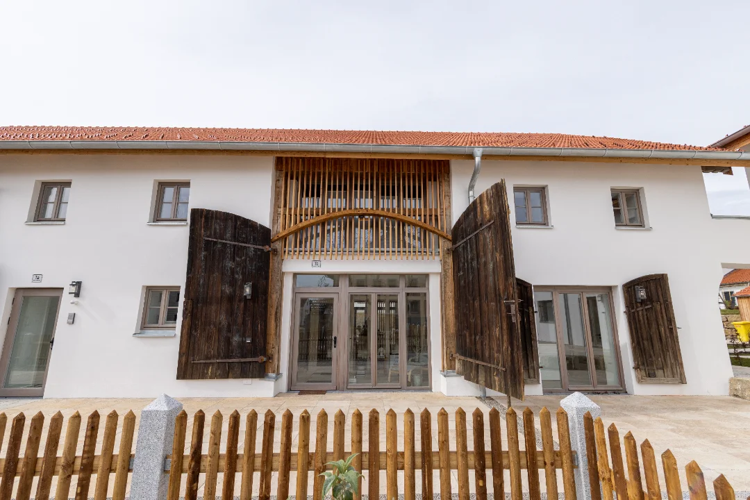 Fassade eines weißen Gebäudes mit offenem Holztor und Dach mit roten Ziegeln.