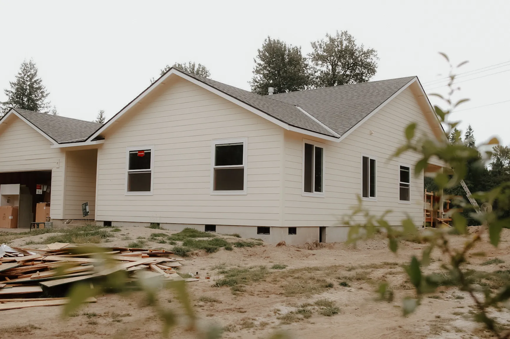 New single-story house with beige siding under construction on a dirt lot with building materials outside.