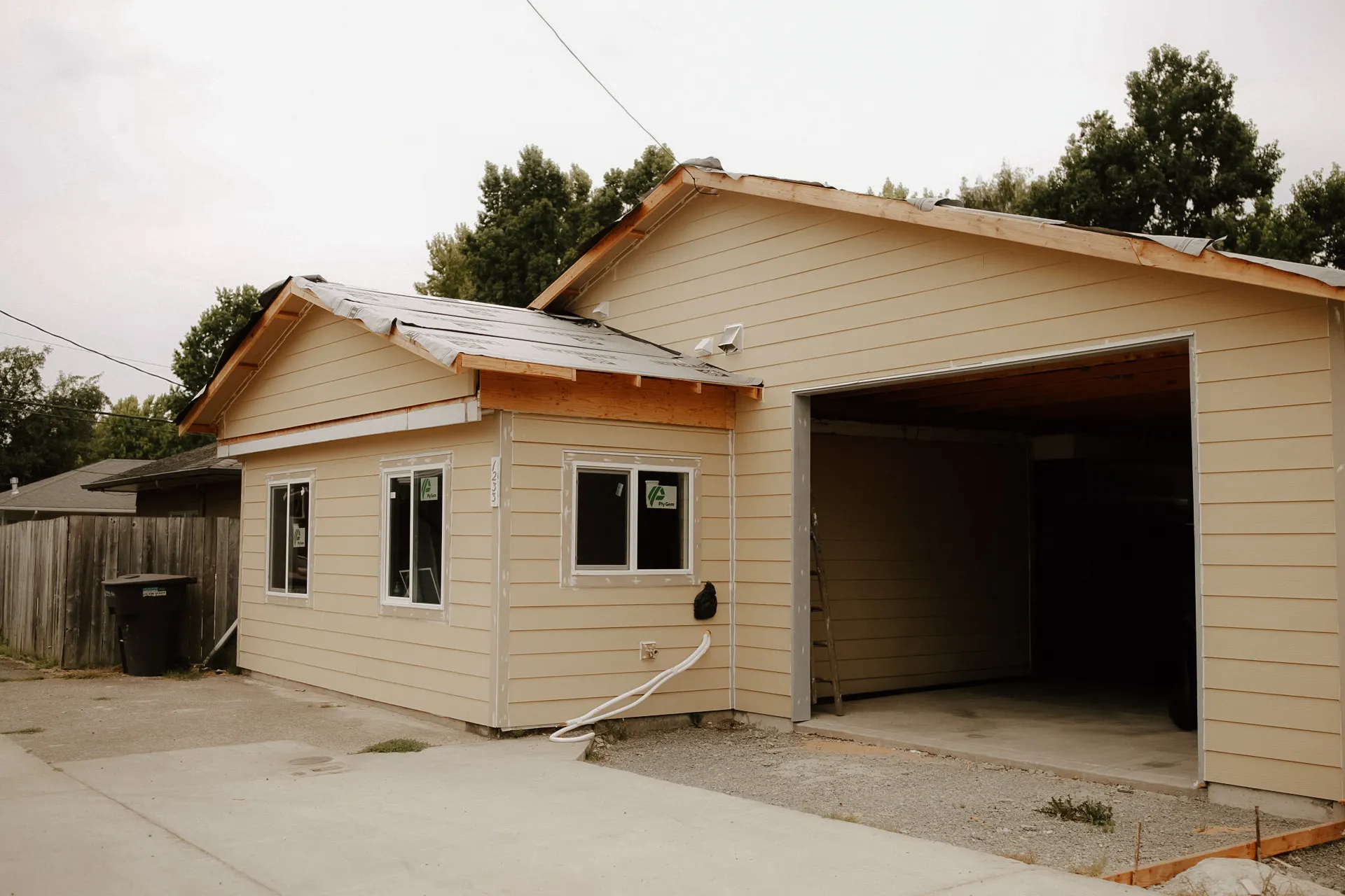 Partially constructed beige house with open garage and unfinished roof on an overcast day.
