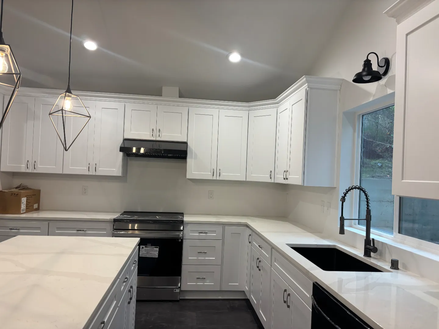 Modern kitchen with white cabinets, marble countertops, black sink, stainless steel stove, and pendant lights.