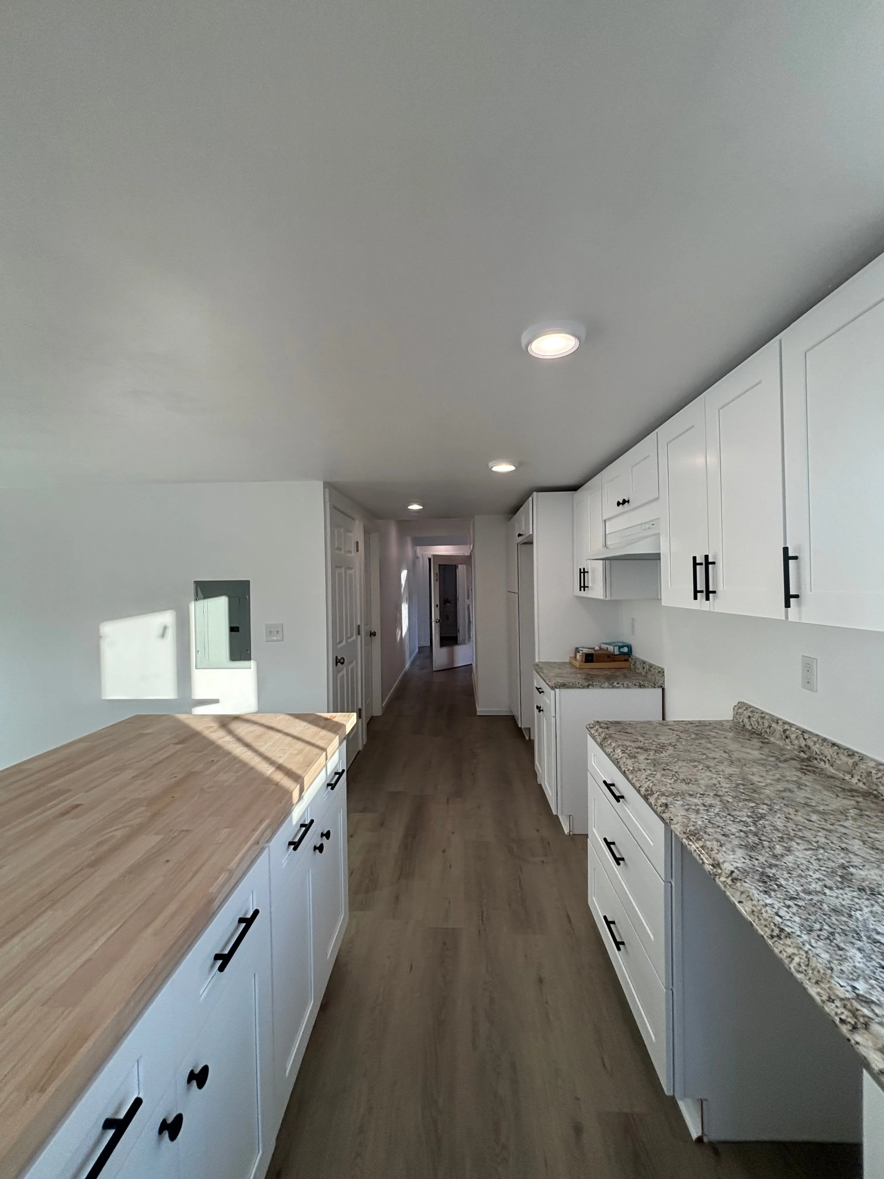Modern kitchen with white cabinets, black handles, wood and granite countertops, and wood flooring.