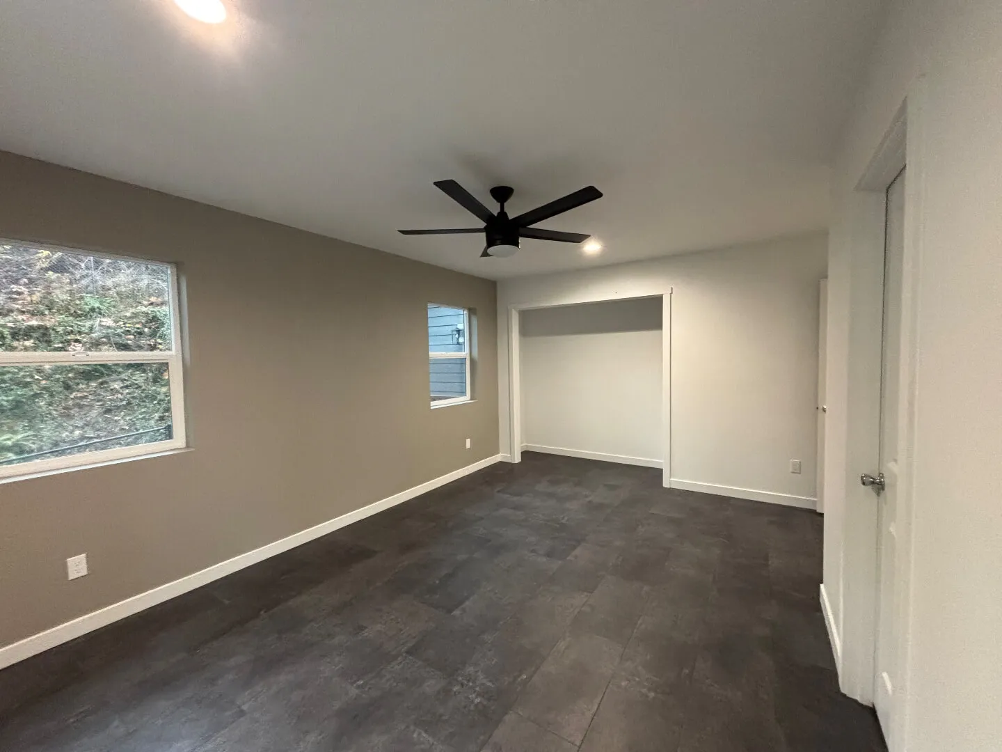 Empty room with grey tiled floor, beige and white walls, two windows, a black ceiling fan, and recessed lighting.