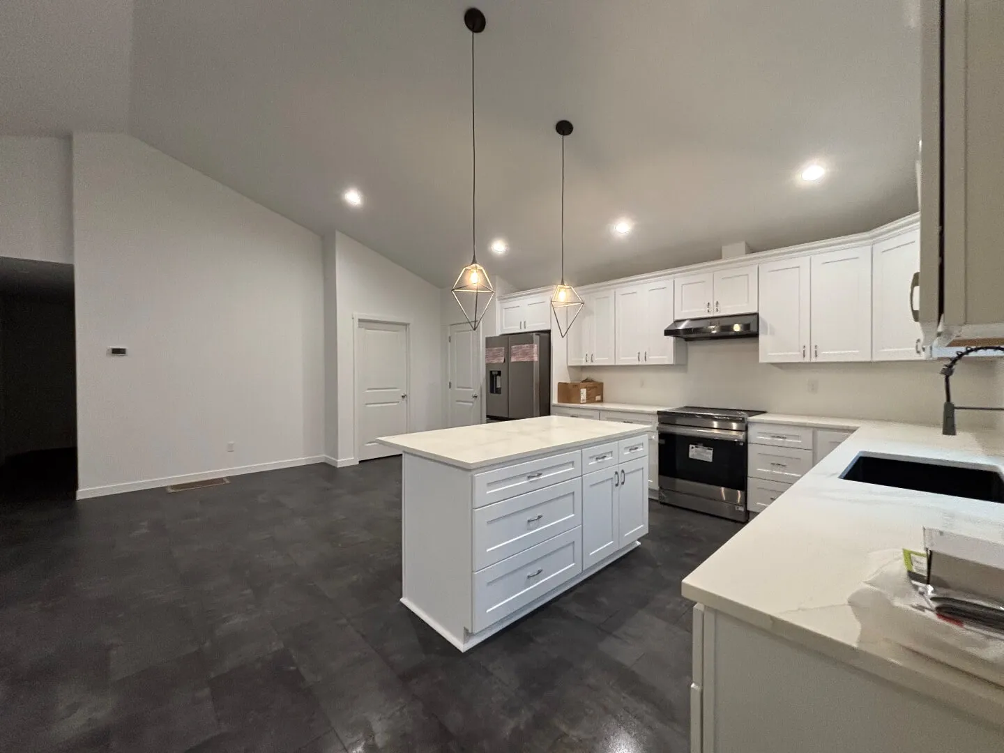 Modern kitchen with white cabinets, a large central island, stainless steel appliances, and dark tile flooring.