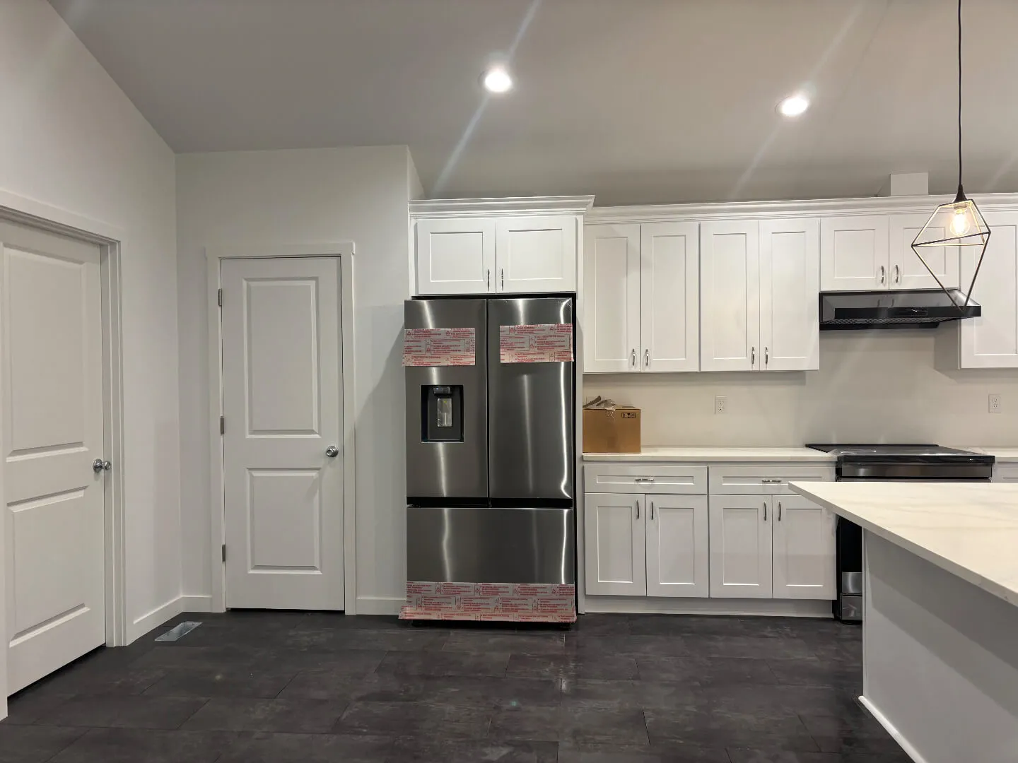 Modern kitchen with white cabinets, stainless steel refrigerator, stove, and a pendant light over the island.