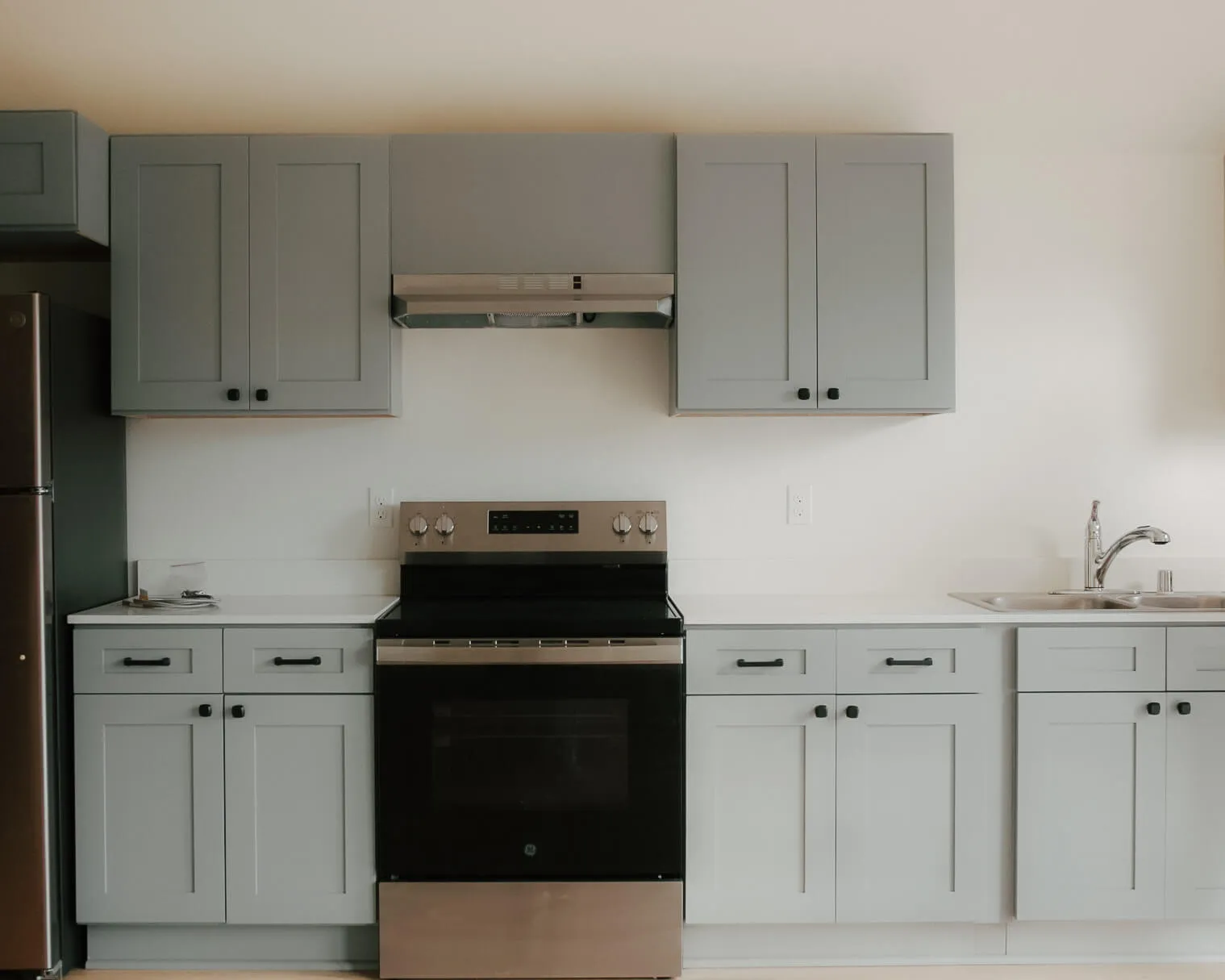 Modern kitchen with light gray cabinets, stainless steel stove, refrigerator, and double sink.