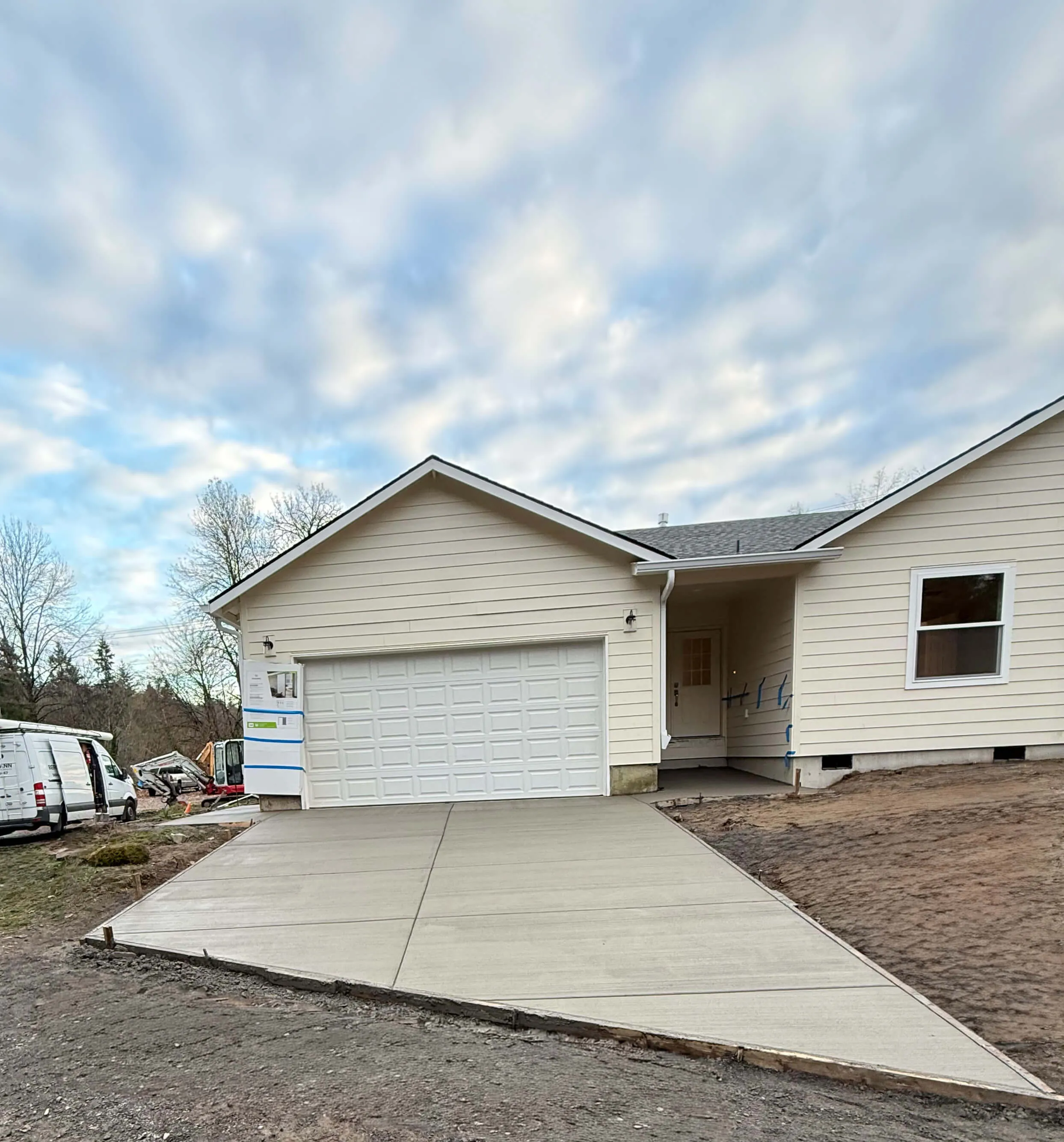 Newly poured concrete driveway leading to a beige single-story house with a white garage door.