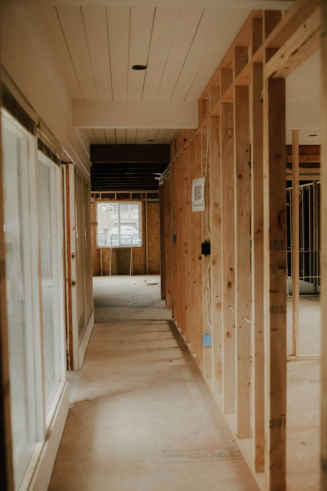 Hallway inside a house under construction with exposed wooden framing and a window at the far end.