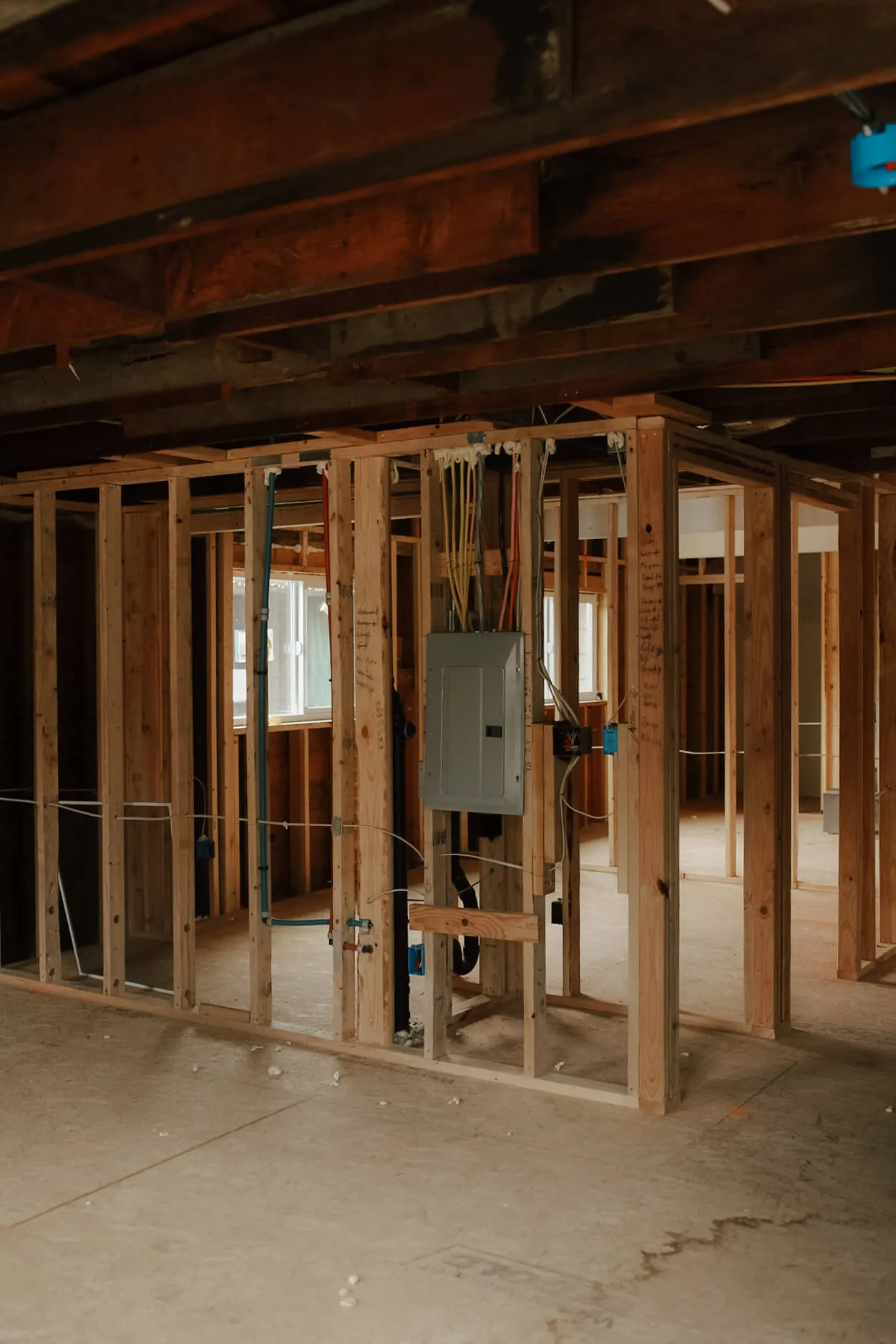 Interior view of a house under construction showing wooden framing and electrical panel with wiring.