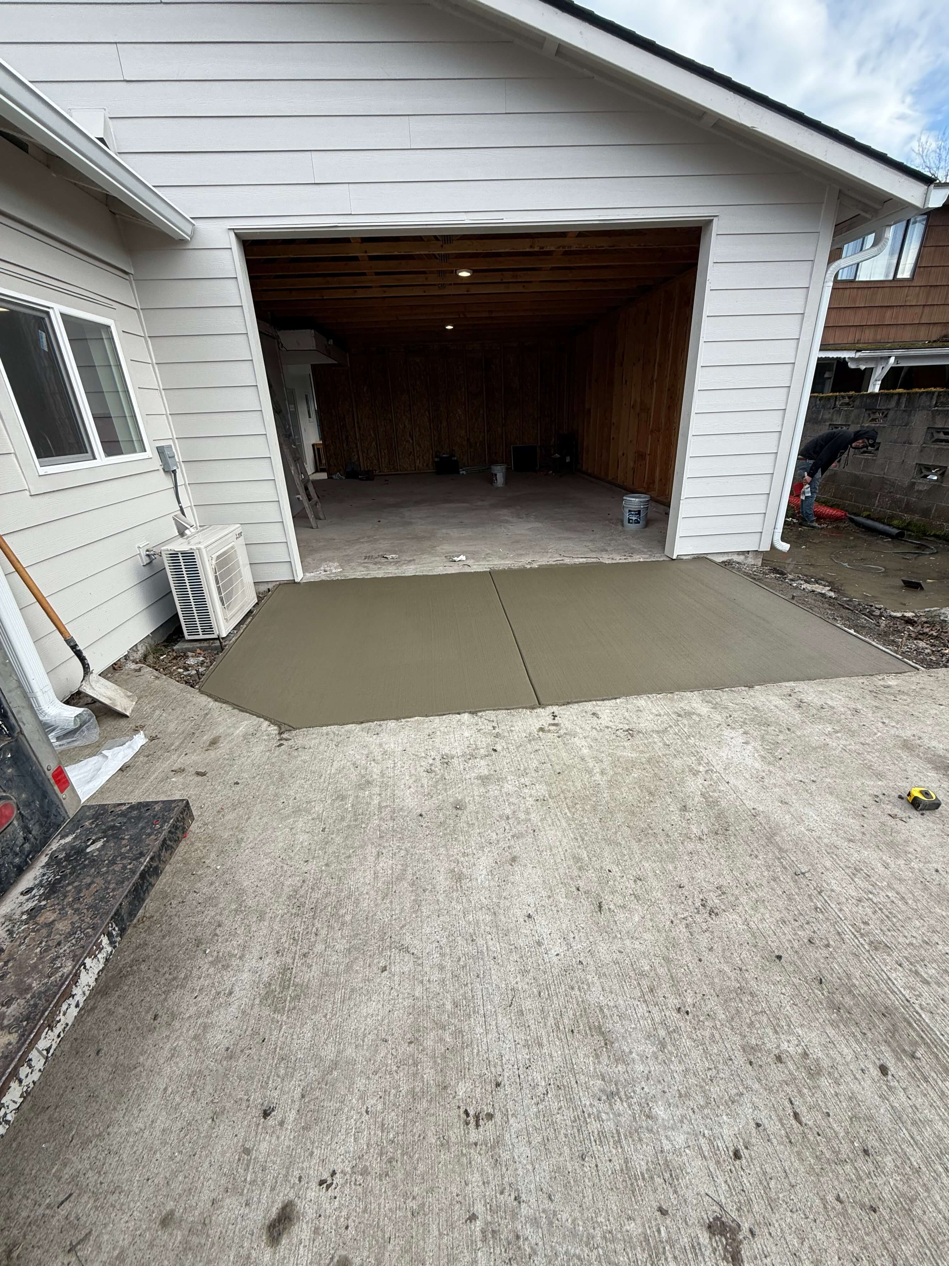 Newly poured concrete slab in front of a garage with open door and unfinished interior walls.