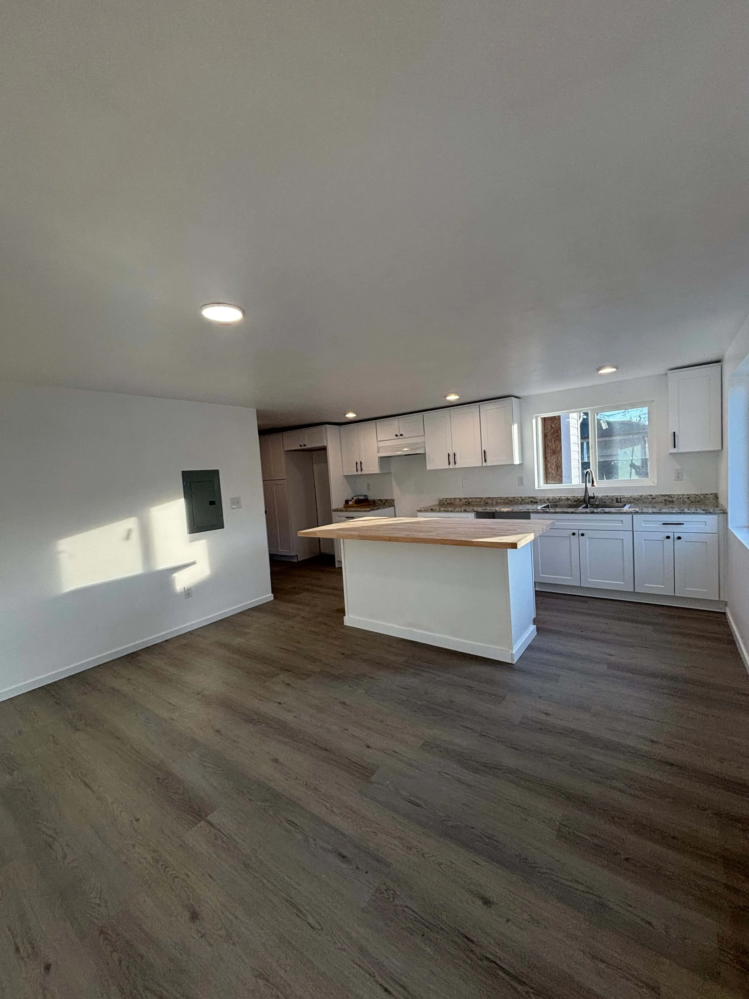 Empty modern kitchen with white cabinets, granite countertops, wooden island, and large window.