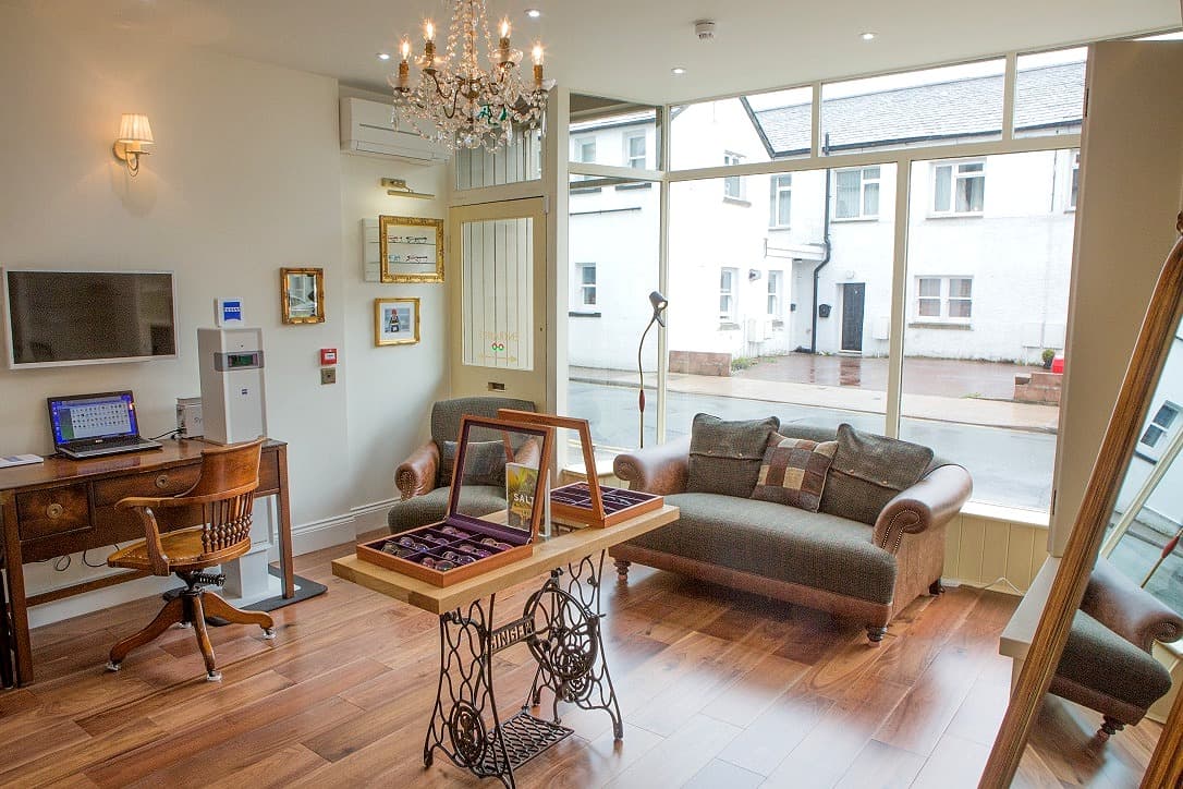 Bright living room with wooden floor, vintage furniture, chandelier, and large windows showing white buildings.