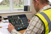 Man in high-visibility vest using a tablet with a home design app near a window.