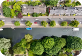 Aerial view of canal with boats, trees, and residential buildings along a road.