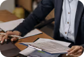 Person in business attire reviewing documents with a pen at a desk.