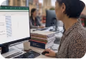 Person working at a desk using a computer with code displayed on the screen in an office setting.