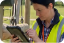 Worker in high-visibility vest using a tablet inside an industrial vehicle cab.
