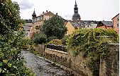 Stone wall-lined water canal with old buildings and a church tower in the background under cloudy sky.