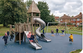 Children playing on a wooden playground with slides and climbing structures in a park.