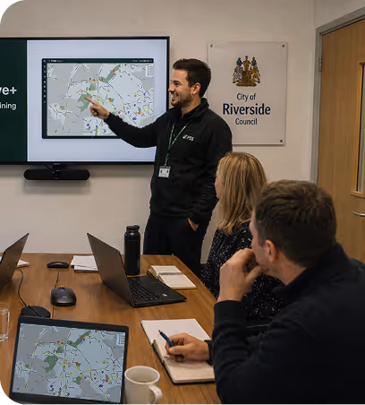 Man presenting a map on screen to two seated colleagues in a City of Riverside Council meeting room.