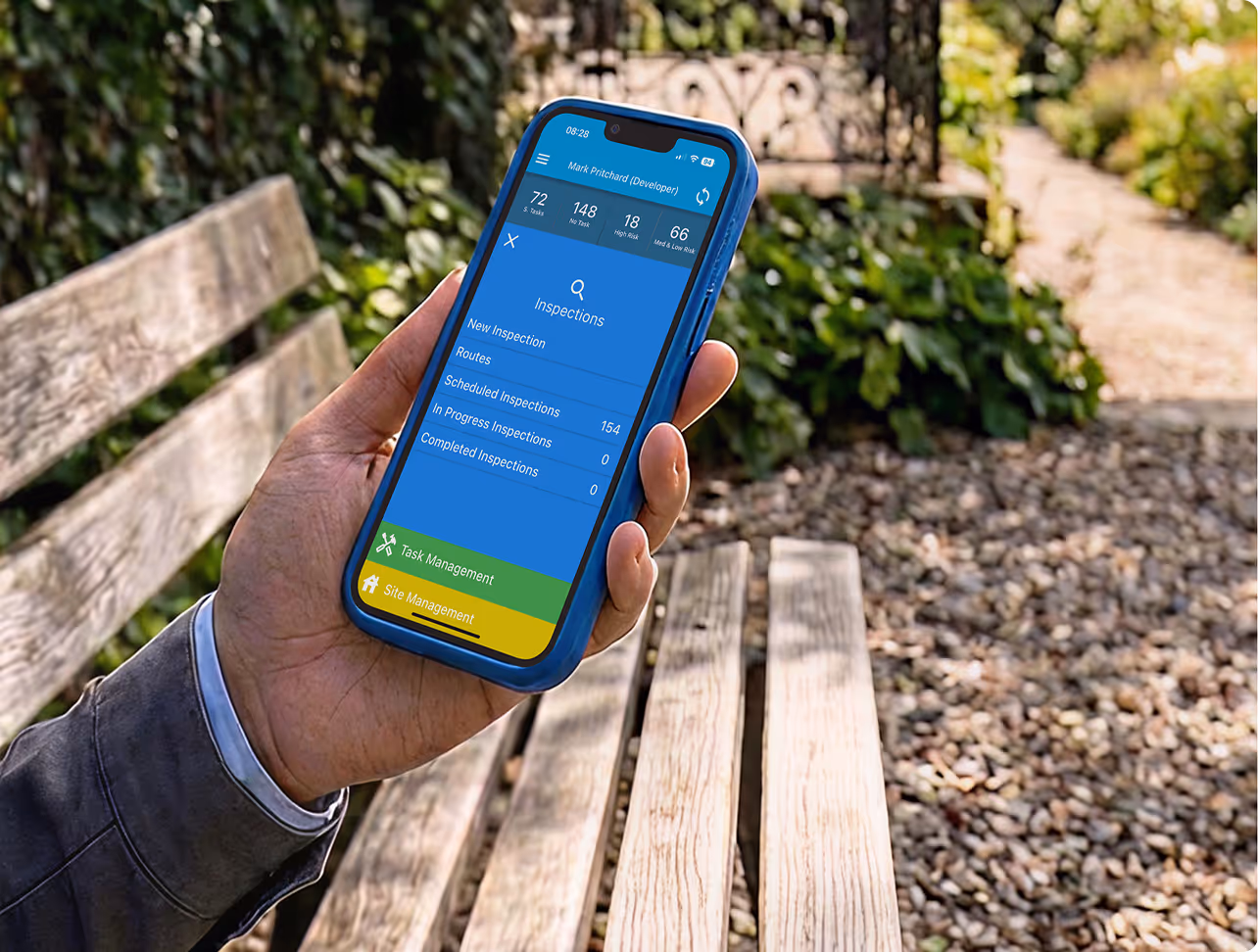 Hand holding smartphone showing an inspections app interface with task and site management options.