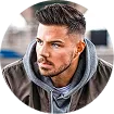 Young man with styled hair and beard wearing a gray hoodie and jacket looking to the side.