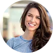 Smiling woman with long brown hair wearing a blue top with blurred background.