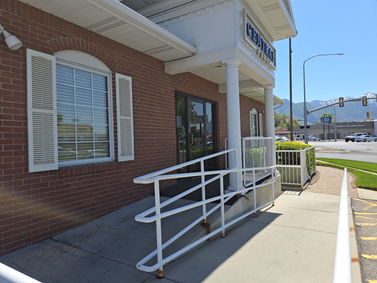 Ramp entrance with white railings to a brick building labeled Central Bank with mountains in the background.
