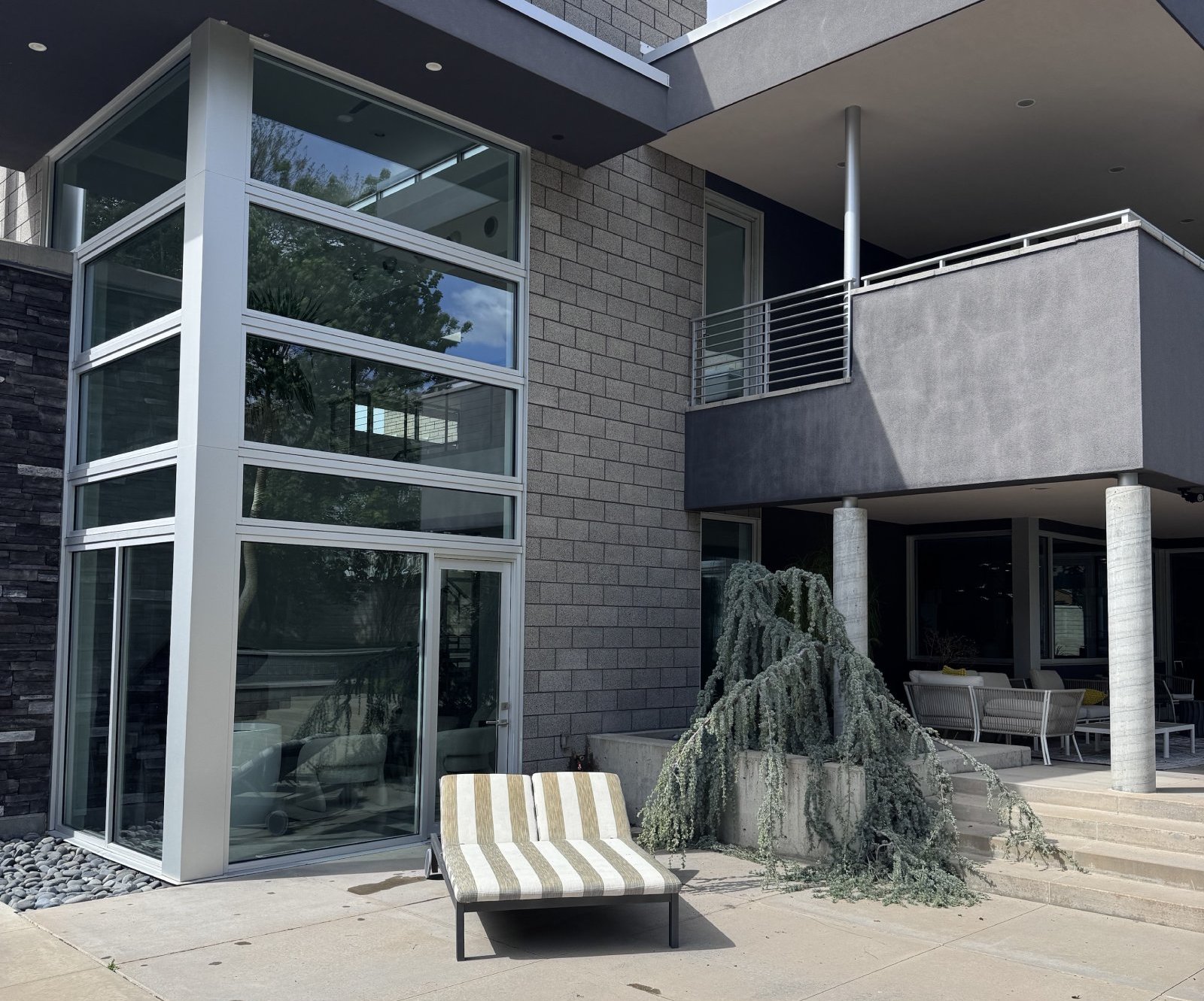 Modern patio with striped lounge chair, concrete steps, and large glass windows on building.