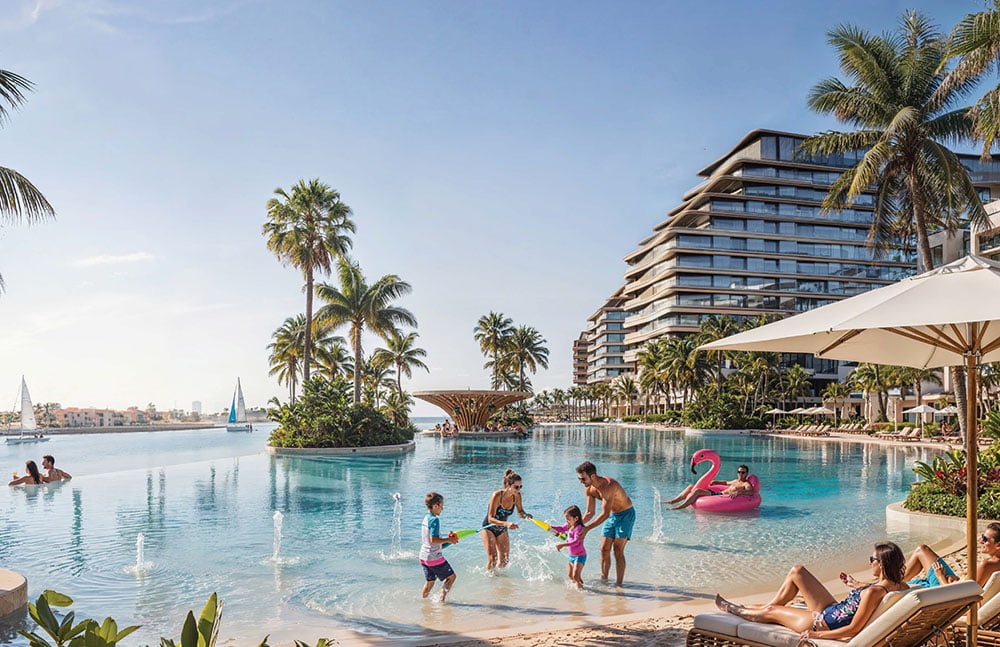 Families and residents enjoying a resort-style swimming pool surrounded by palm trees and modern apartment buildings