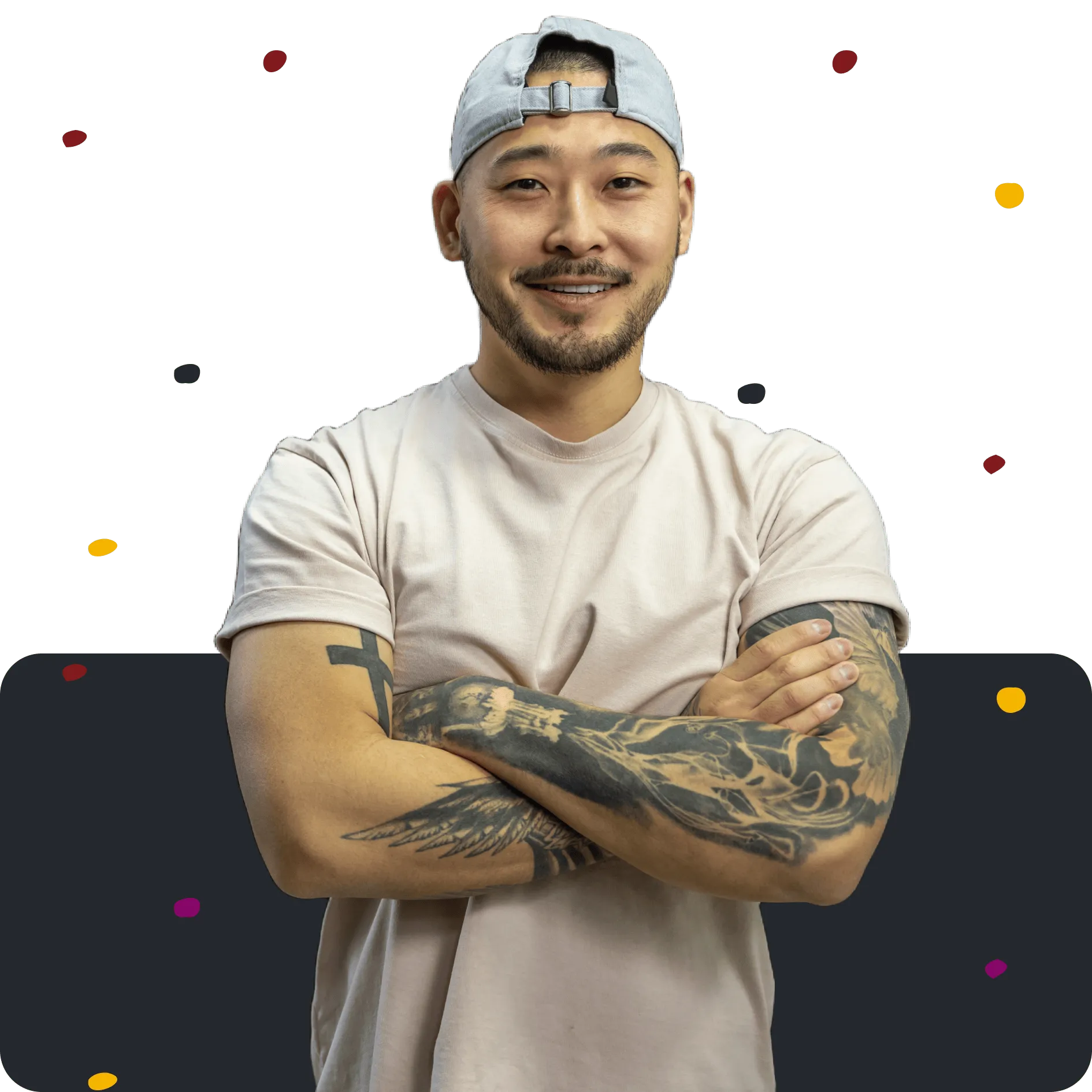 Smiling man with tattoos on both arms, wearing a beige t-shirt and a backward gray cap.