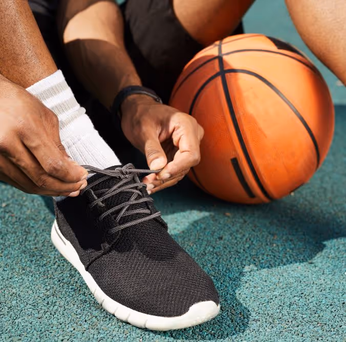 Person tying black athletic shoe laces on a basketball court with an orange basketball nearby.