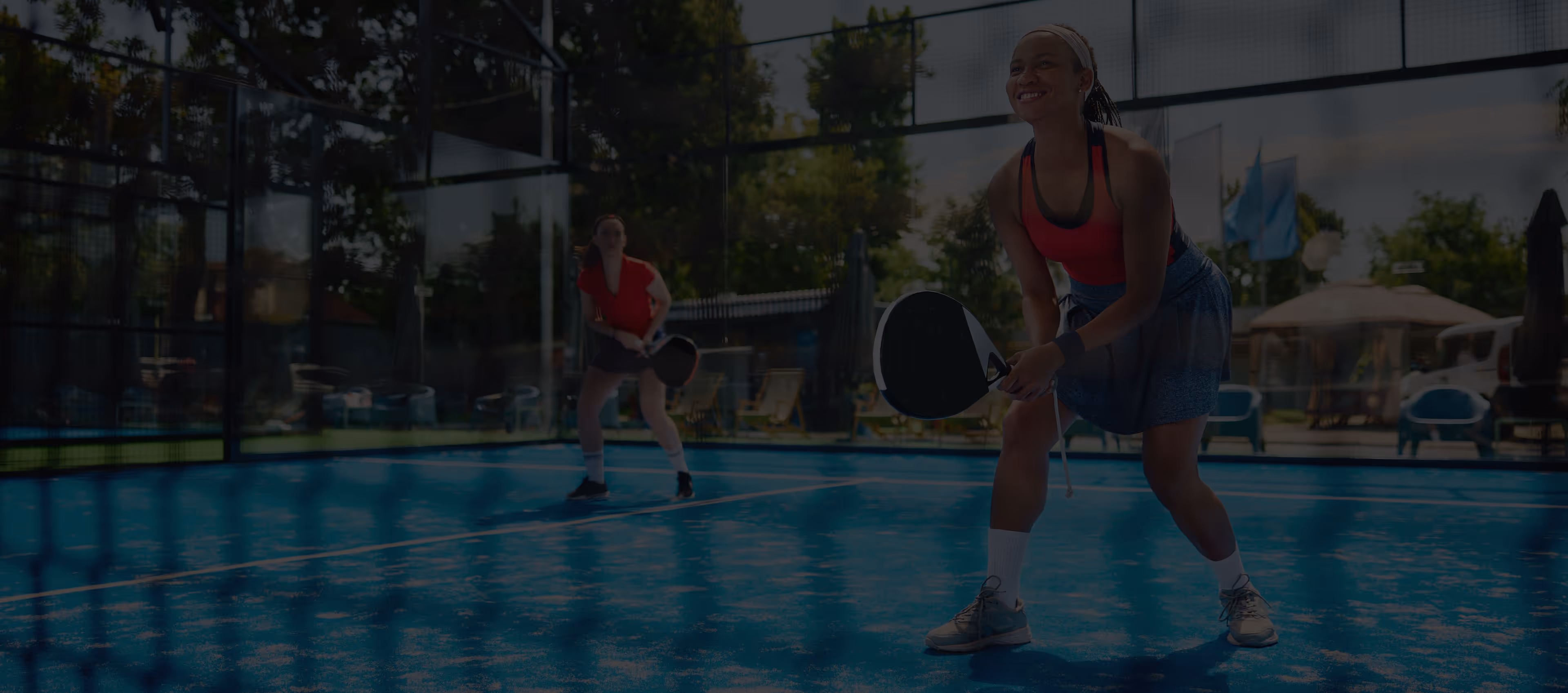 Two women playing pickleball on a blue court with paddles, one preparing to hit the ball.