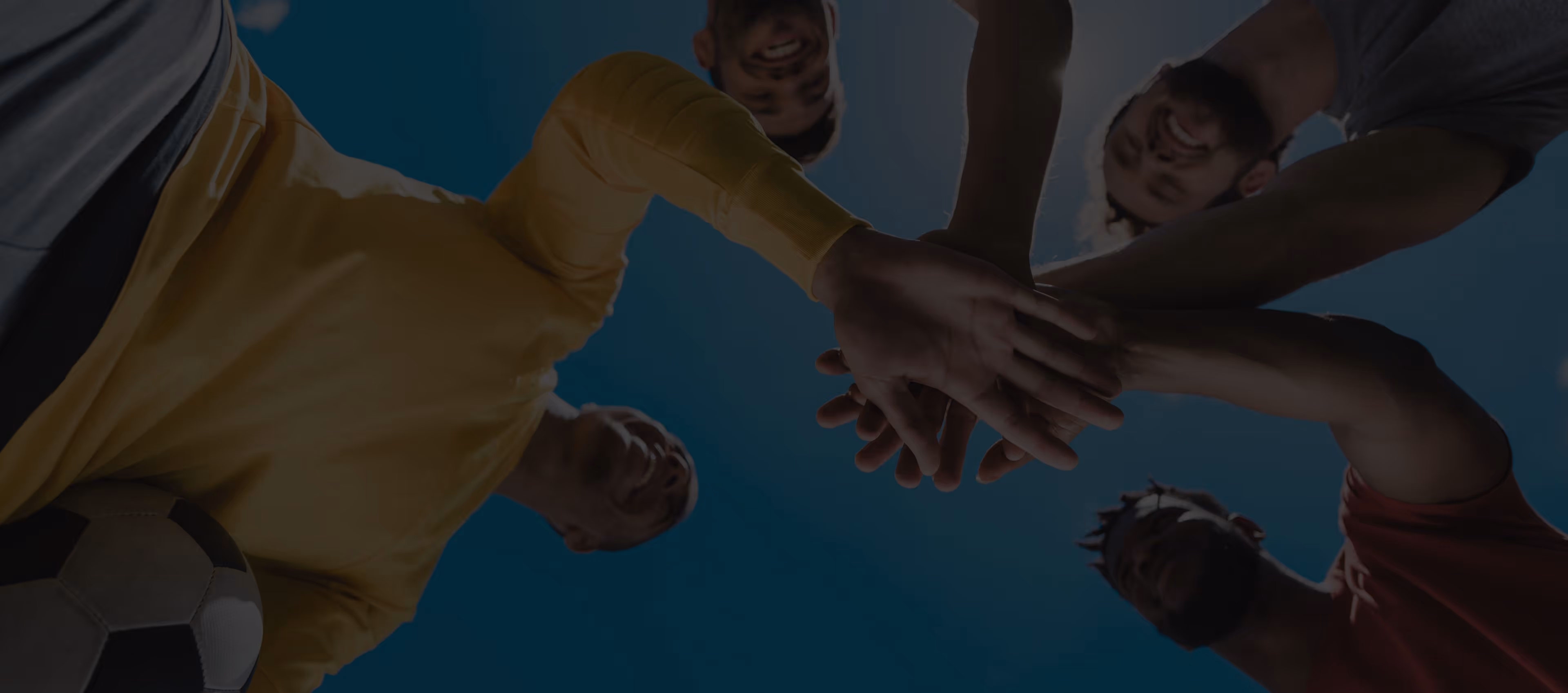 Group of five men in sportswear putting their hands together in a circle over a soccer ball.
