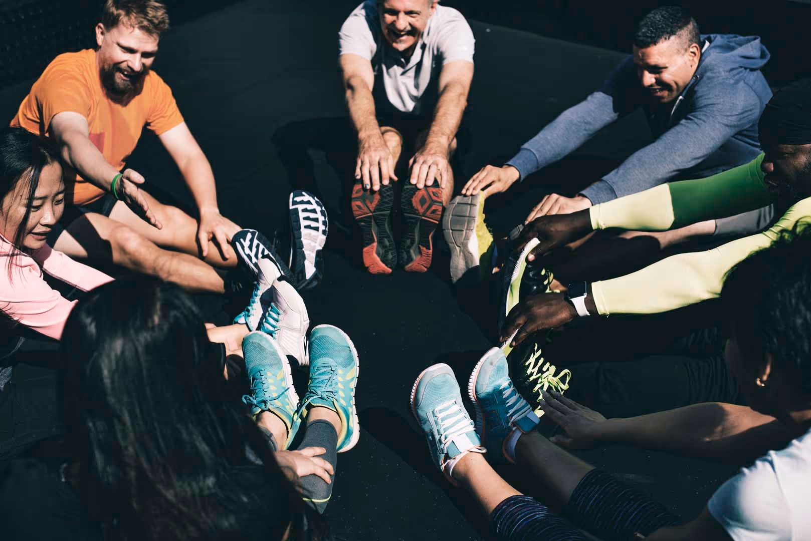 Group of people sitting in a circle stretching their legs and reaching for their feet in a gym.