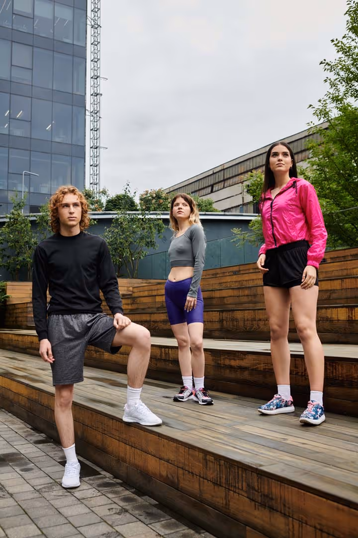 Three young athletes standing on wooden steps in outdoor urban setting wearing workout clothes.