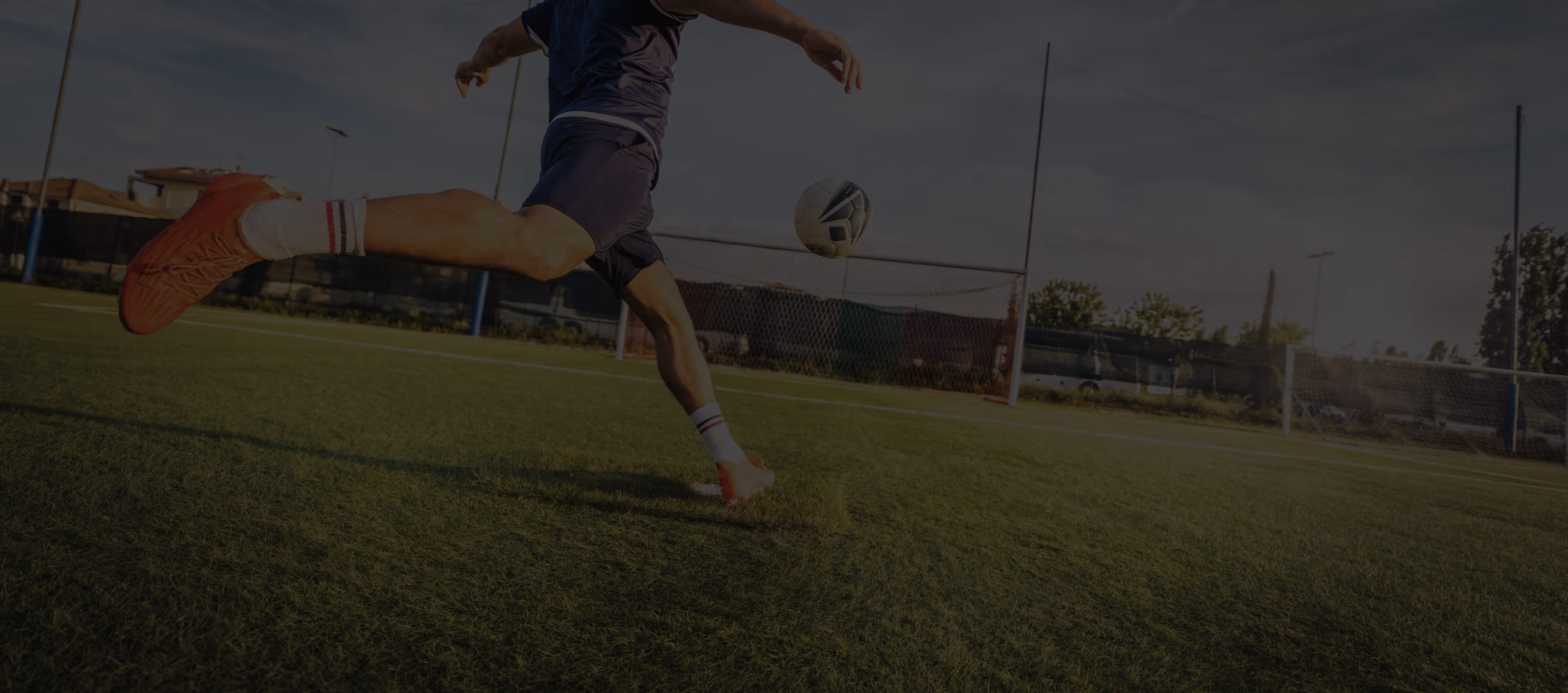 Soccer player in mid-kick on a grassy field aiming at the goal during sunset.