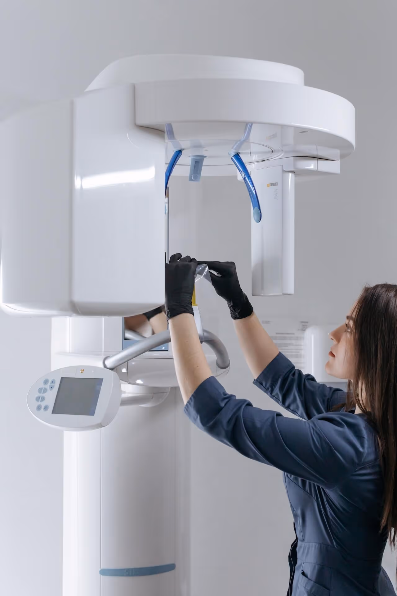 Woman in blue medical uniform adjusting a dental panoramic X-ray machine in a clinical setting.