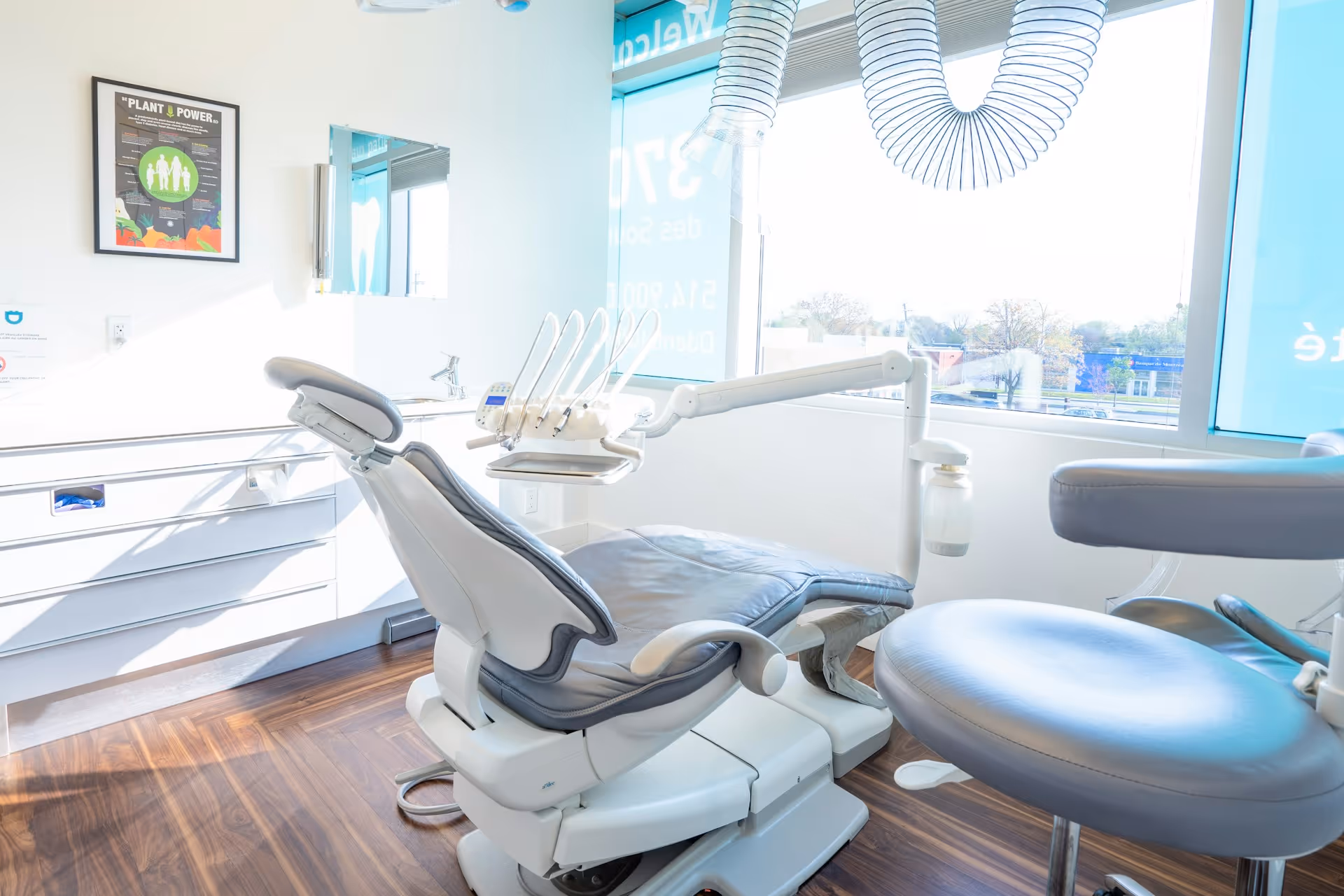 Modern dental office with a blue dental chair, overhead light, and dental equipment against white walls and wooden floor.